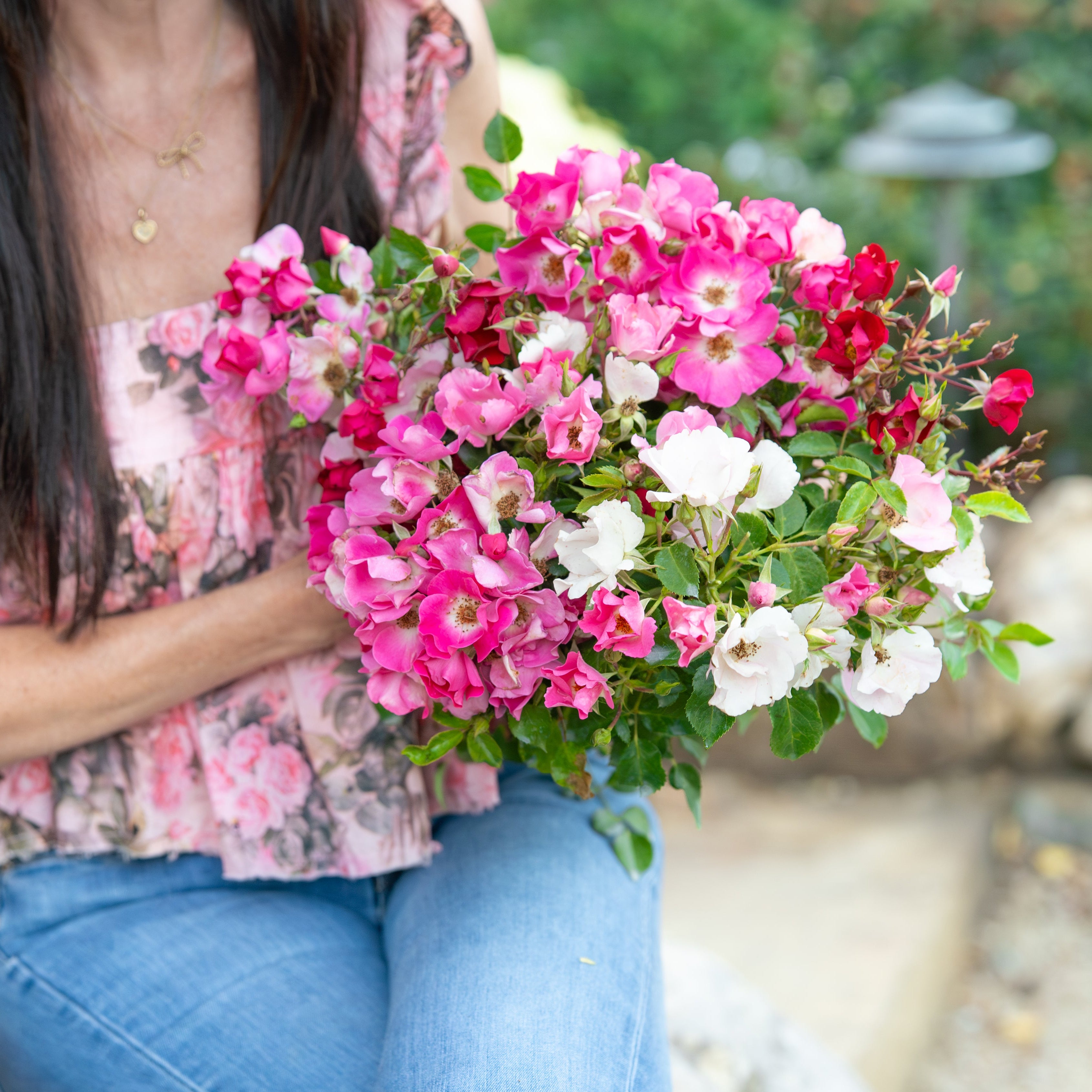 Person holding a bouquet of pink, white, and red flowers outdoors.