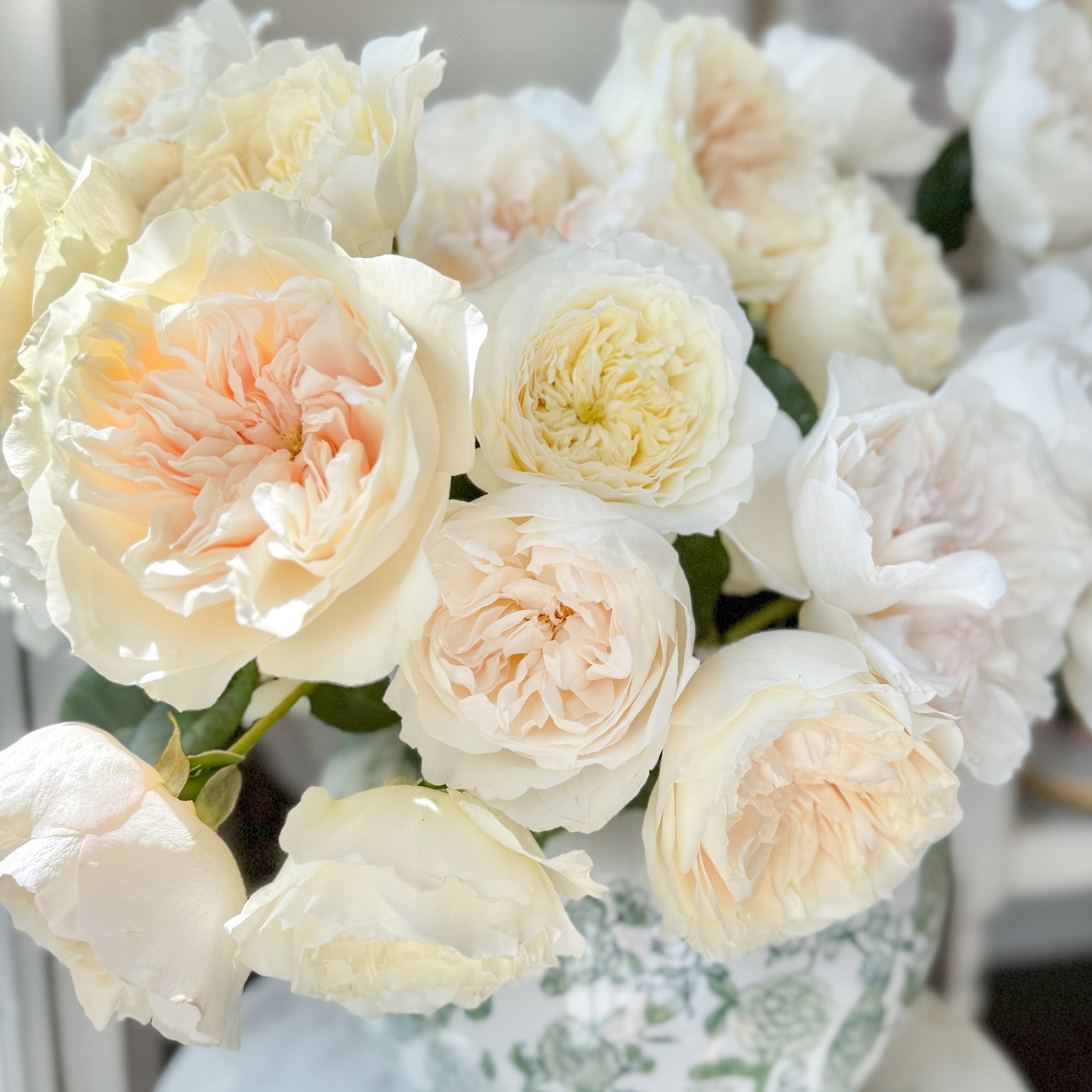 Bouquet of white and light pink roses in a decorative vase on a marble surface.