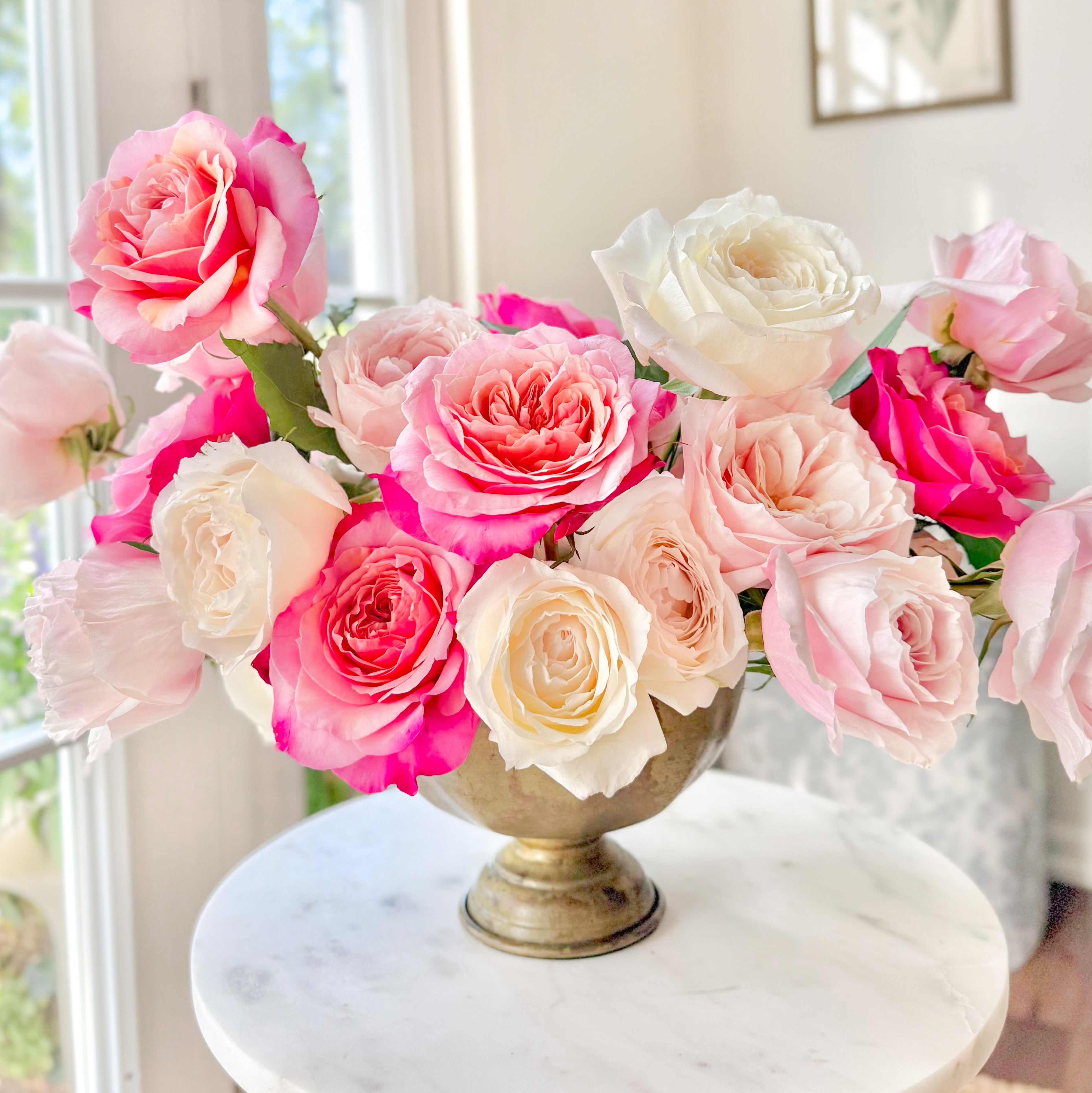 Bouquet of pink, white, and peach roses in a gold vase on a marble table.