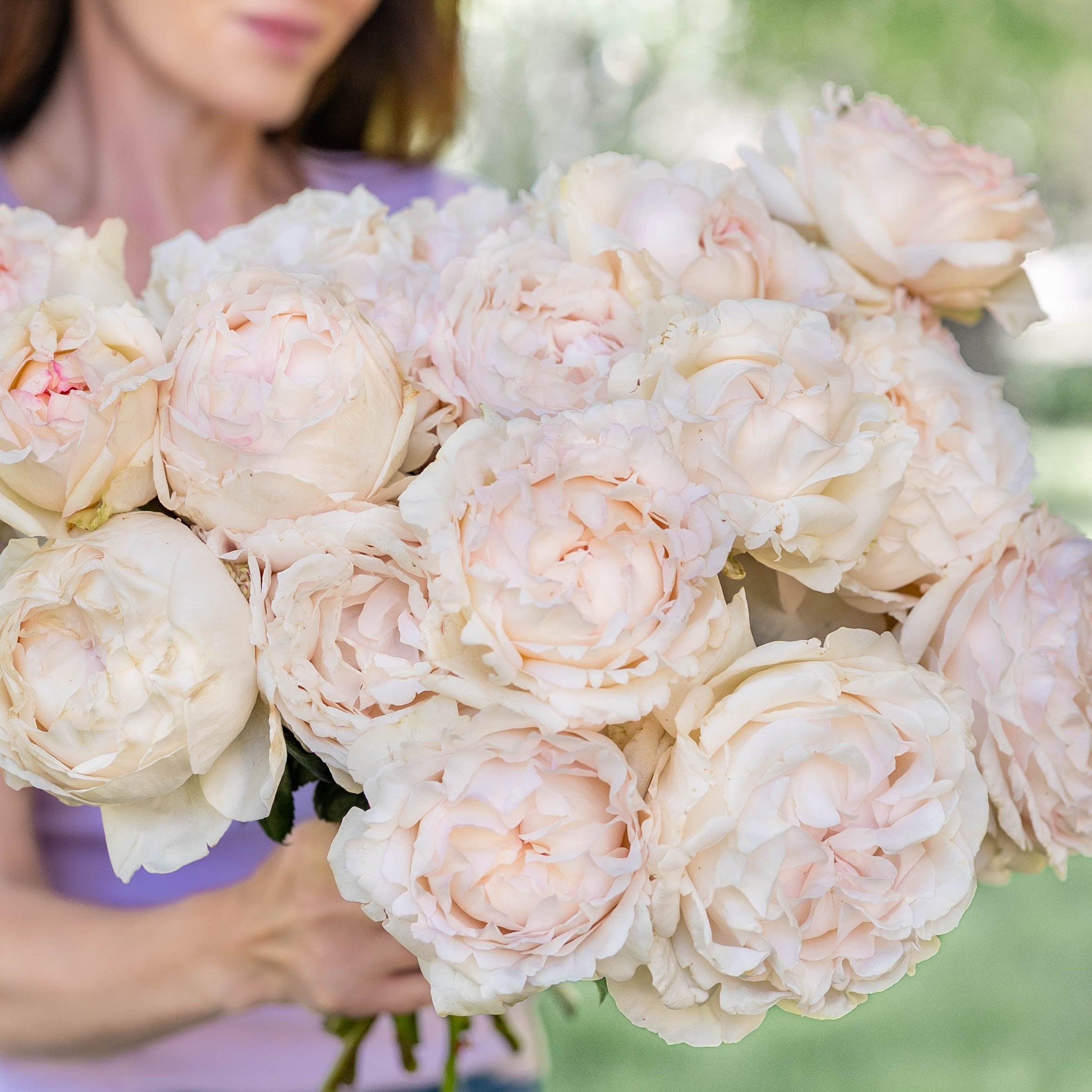 Woman holding a bouquet of white flowers outdoors with greenery in the background